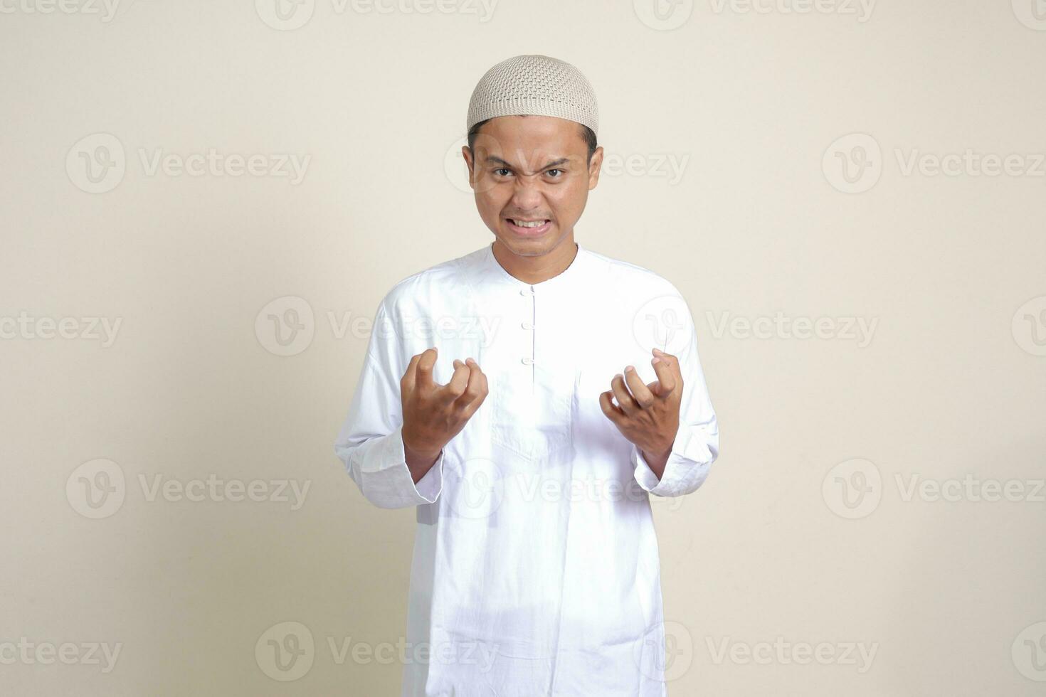 Portrait of attractive Asian muslim man in white shirt making angry hand gesture with fingers. Isolated image on gray background photo