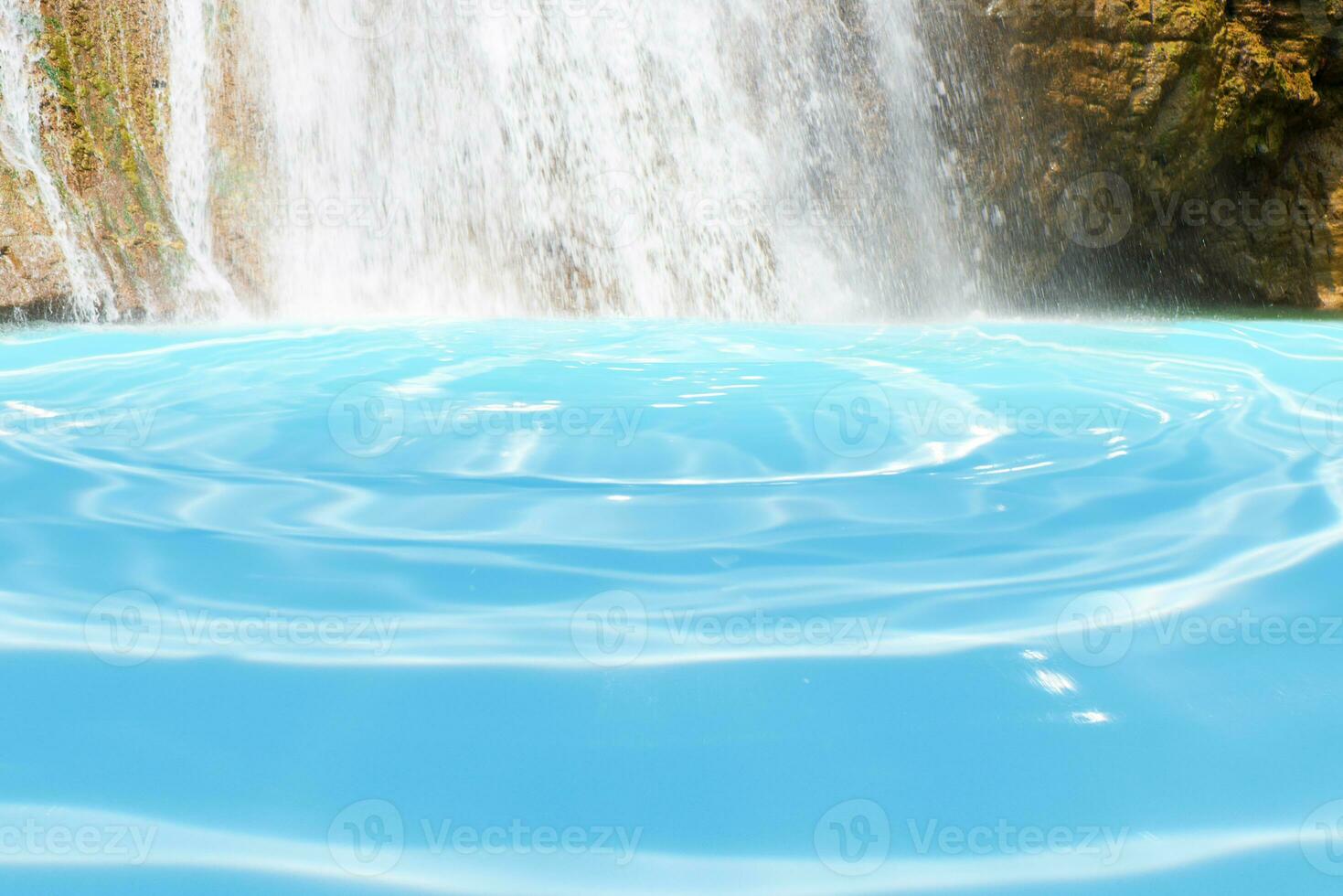 Beautiful waterfall in forestry with blue water with ripples on the surface. Blurred transparent blue colored clear calm water surface texture with splashes and bubbles. Water waves with shining. photo