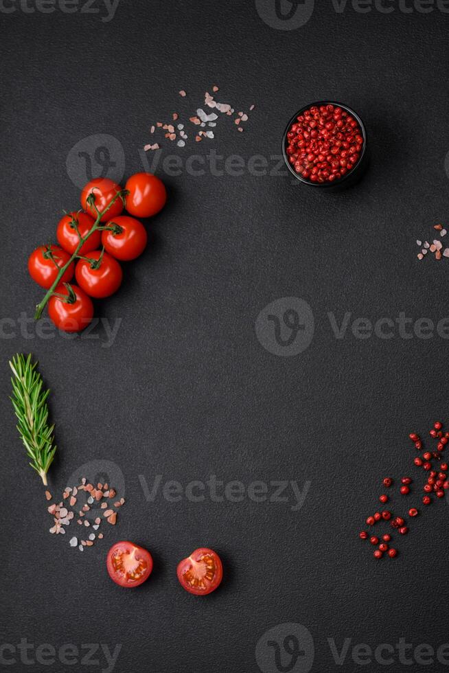 Empty black texture table, cherry tomatoes on a twig, spices, salt and herbs photo