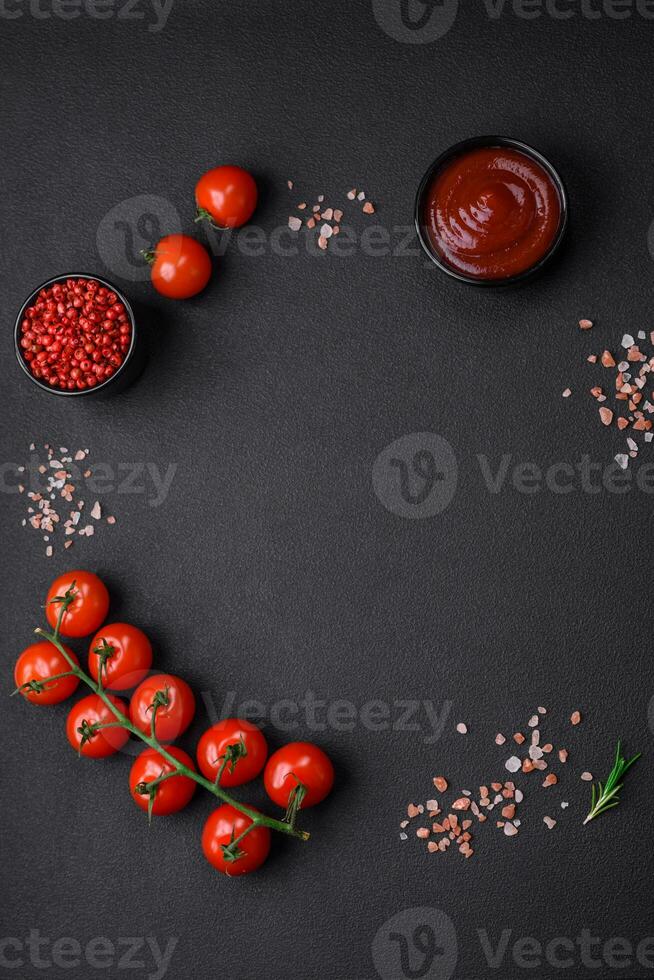 Empty black texture table, cherry tomatoes on a twig, spices, salt and herbs photo