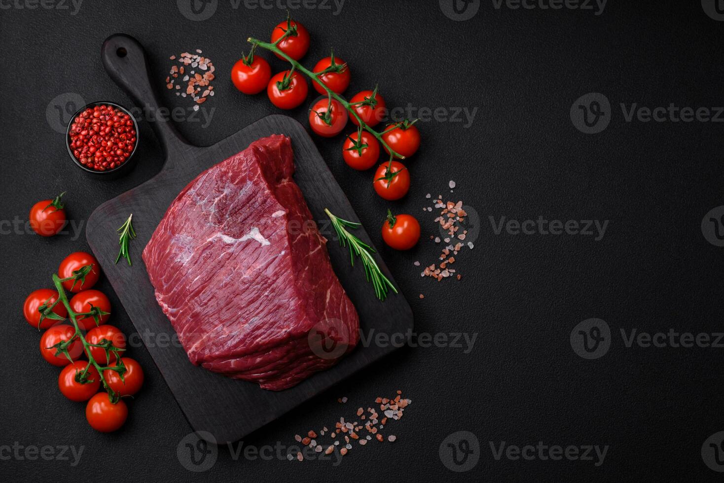 A piece of fresh raw beef with salt, spices and herbs on a wooden cutting board photo