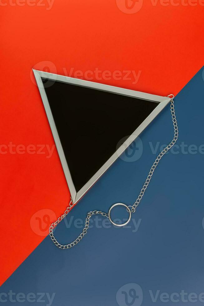 top view of triangle mirror in silver frame on a color blue and red background. Creative backdrop photo