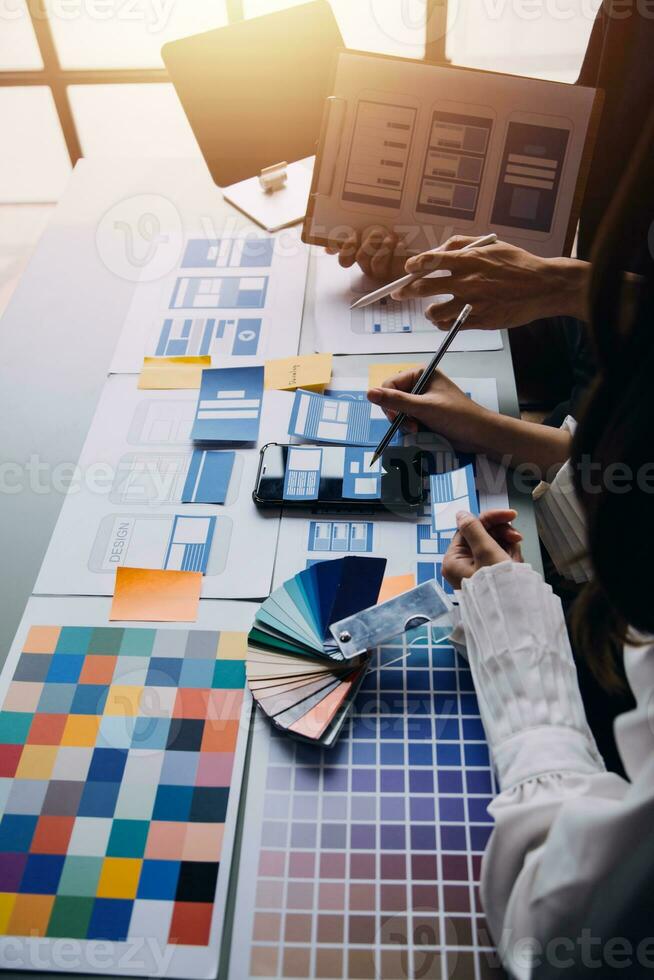 Close up ux developer and ui designer brainstorming about mobile app interface wireframe design on table with customer breif and color code at modern office.Creative digital development agency photo
