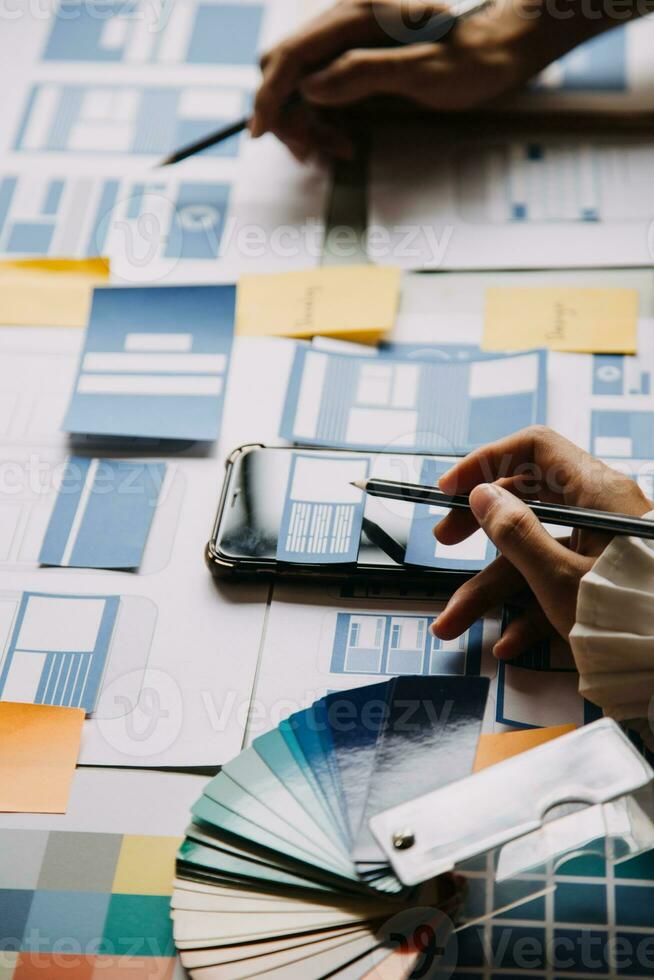 Close up ux developer and ui designer brainstorming about mobile app interface wireframe design on table with customer breif and color code at modern office.Creative digital development agency photo