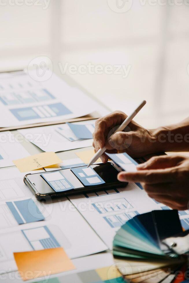 Close up ux developer and ui designer brainstorming about mobile app interface wireframe design on table with customer breif and color code at modern office.Creative digital development agency photo