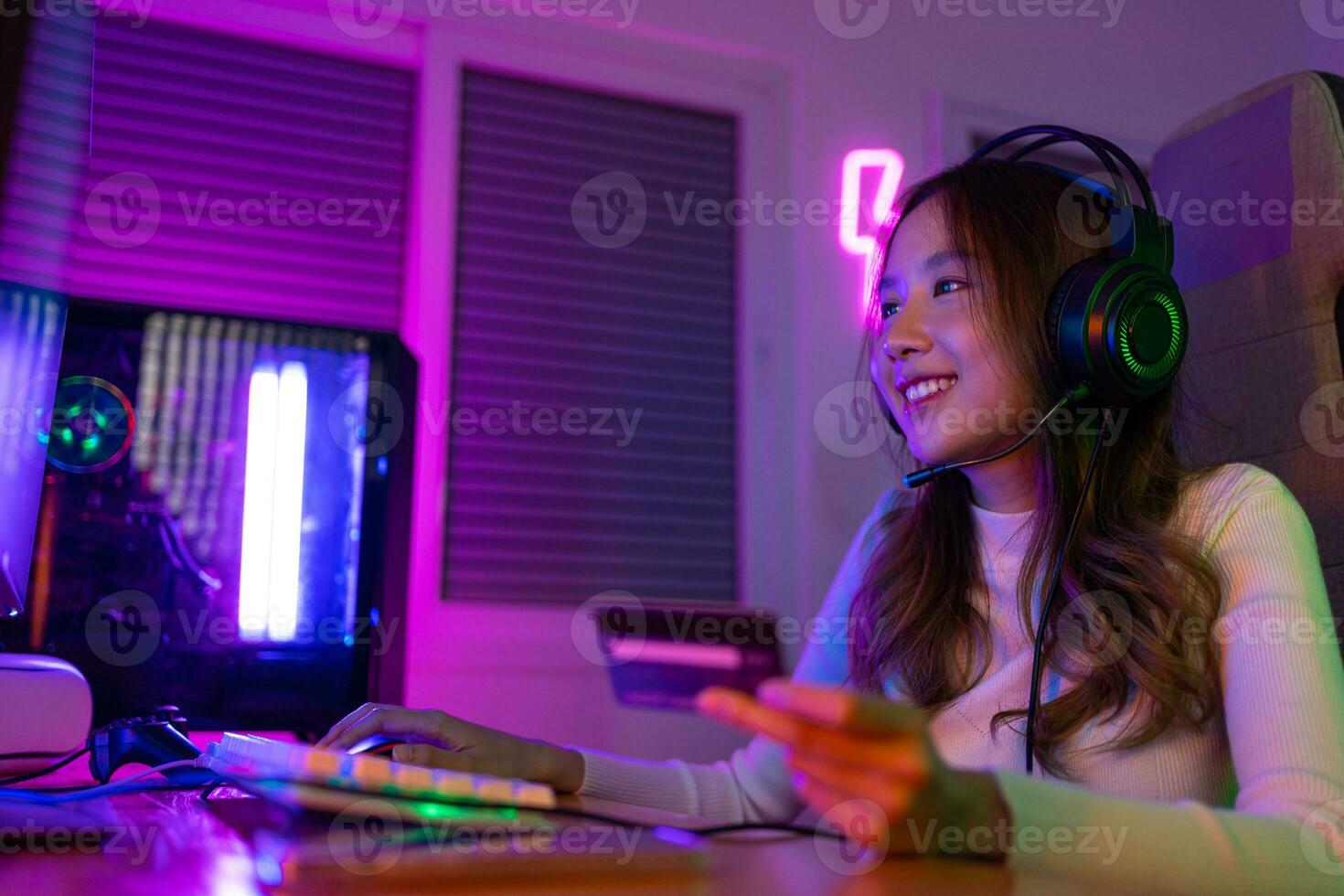 Top up online game with credit card concept. Gamer and E-Sport online of Asian woman playing online computer video game with lighting effect, broadcast streaming live at home. Gamer and E-Sport gaming photo