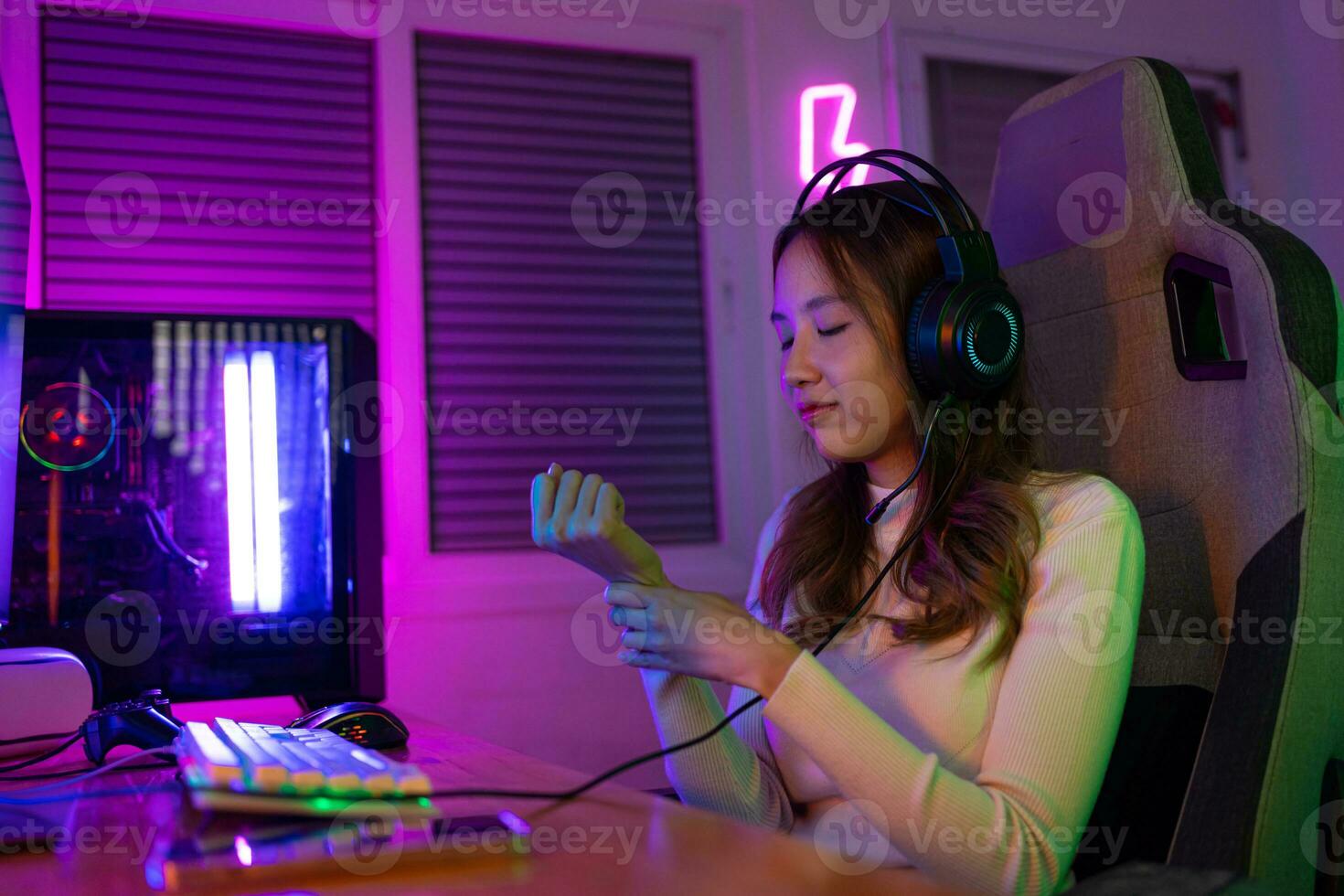 Wrist pain concept. Gamer and E-Sport online of Asian woman playing online computer video game with lighting effect, broadcast streaming live at home. her use her wrist for a long time. photo