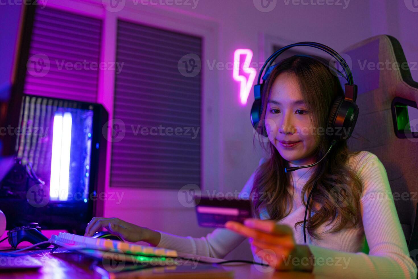 Top up online game with credit card concept. Gamer and E-Sport online of Asian woman playing online computer video game with lighting effect, broadcast streaming live at home. Gamer and E-Sport gaming photo