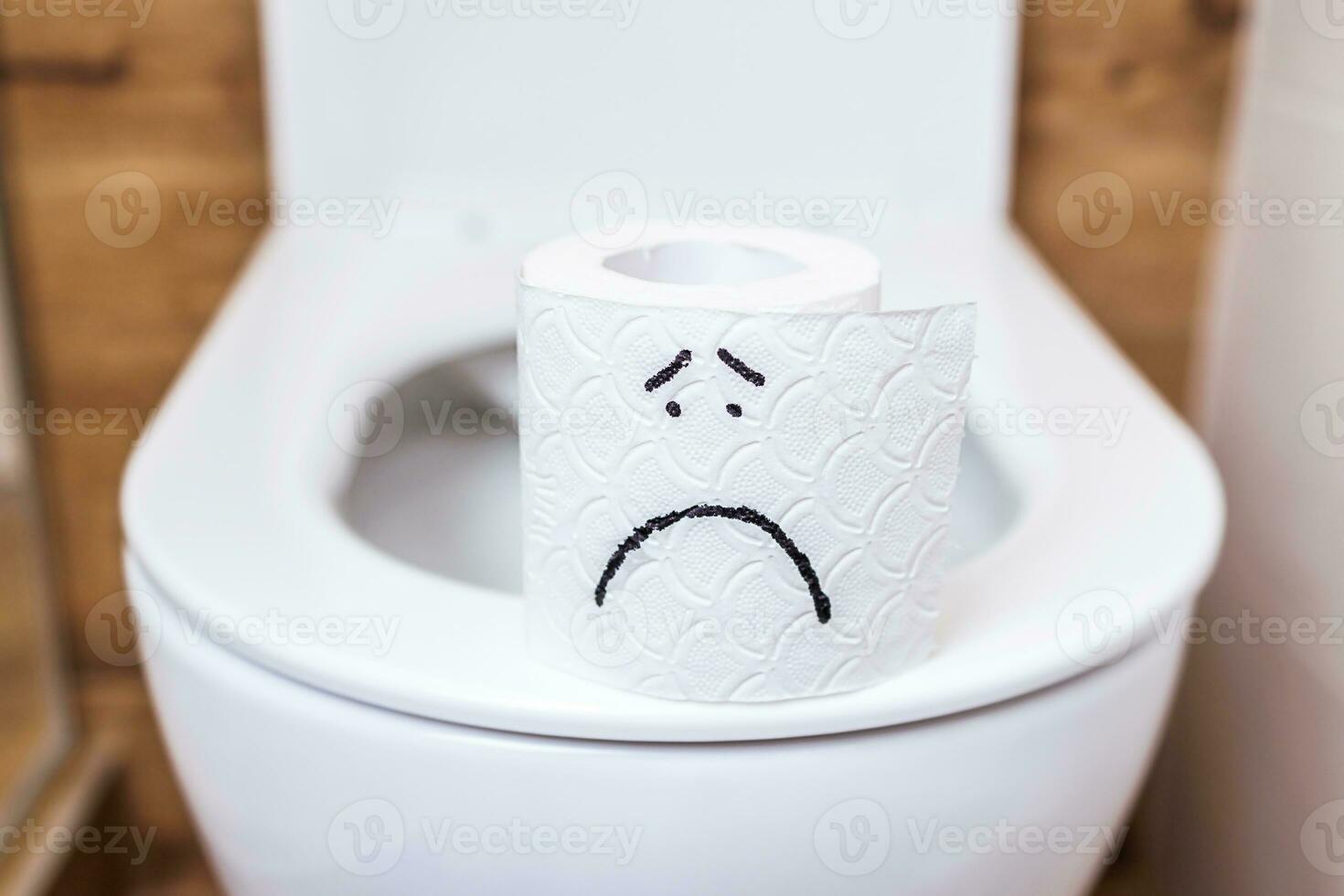 close-up, a roll of toilet paper with a painted sad face stands on the toilet photo
