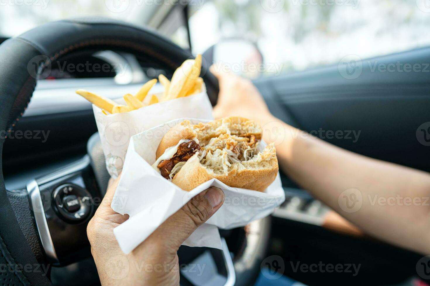 Asian lady holding hamburger and French fries to eat in car, dangerous and risk an accident. photo