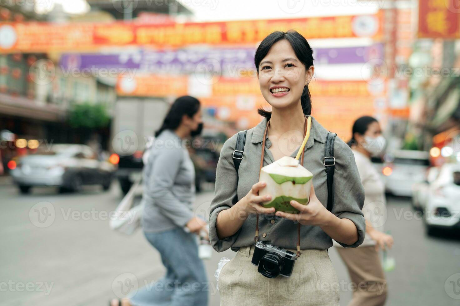 Happy young Asian woman backpack traveler drinking a coconut juice at China town street food market in Bangkok, Thailand. Traveler checking out side streets. photo