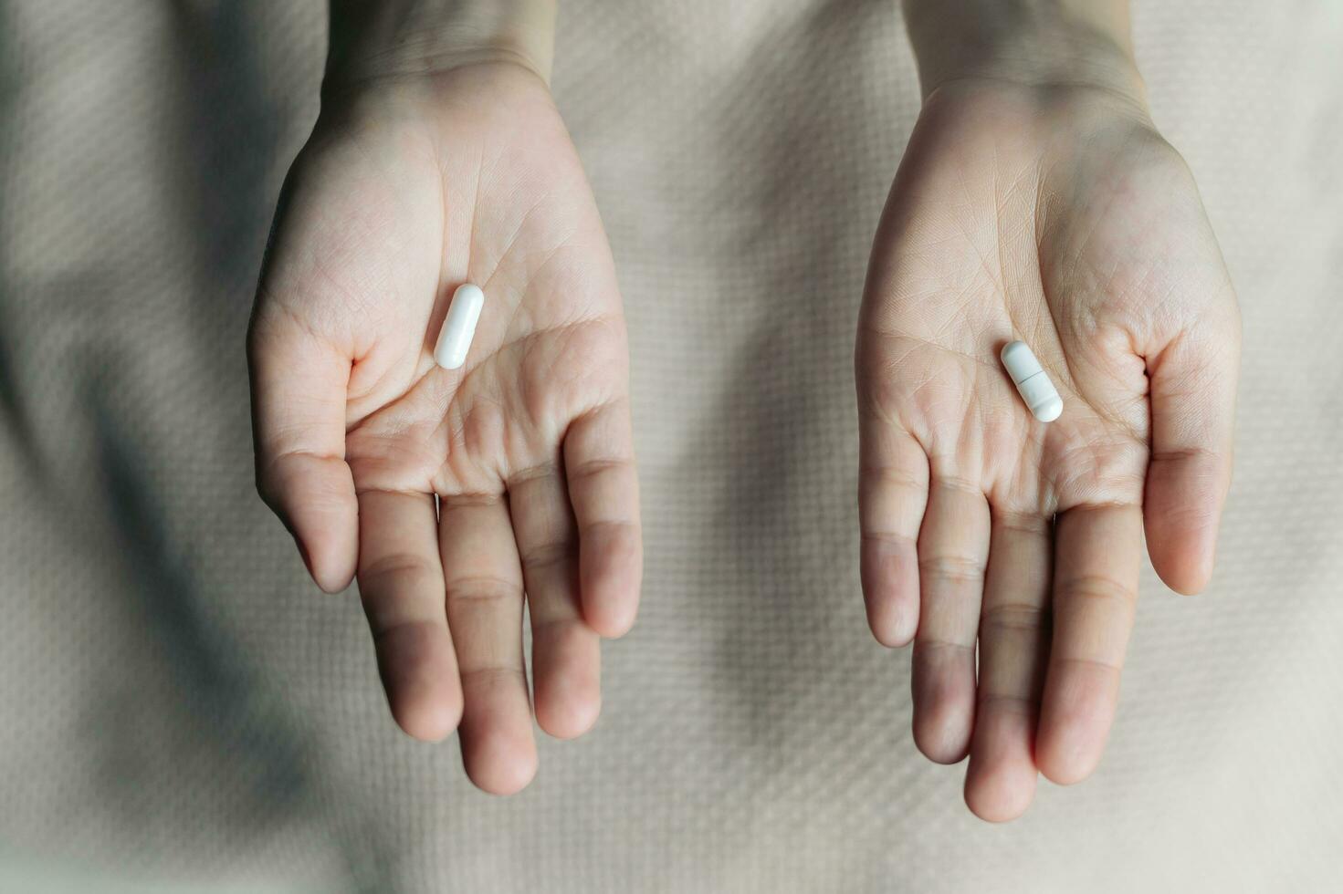 Female hands hold and offer two choice medicine pills capsule for chosen. White and pink candy or meds compare to choose from. Concept decision making or indecisiveness. photo