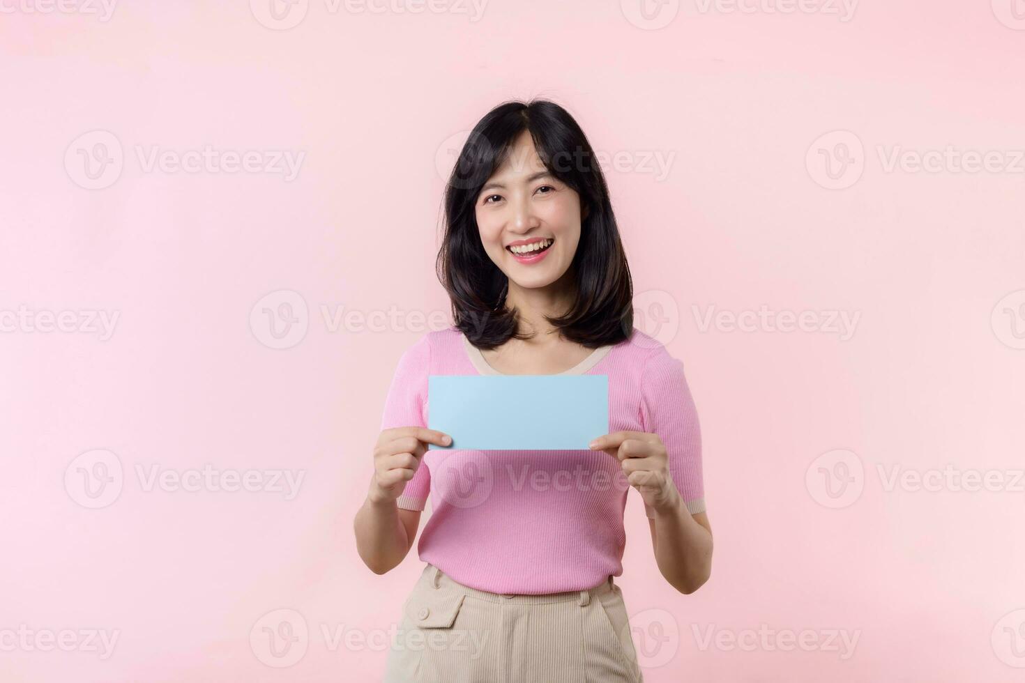 Portrait happy young woman model holding and showing blank space paper for advertisement information message poster with thumb up or point finger gesture isolated on pink pastel studio background. photo