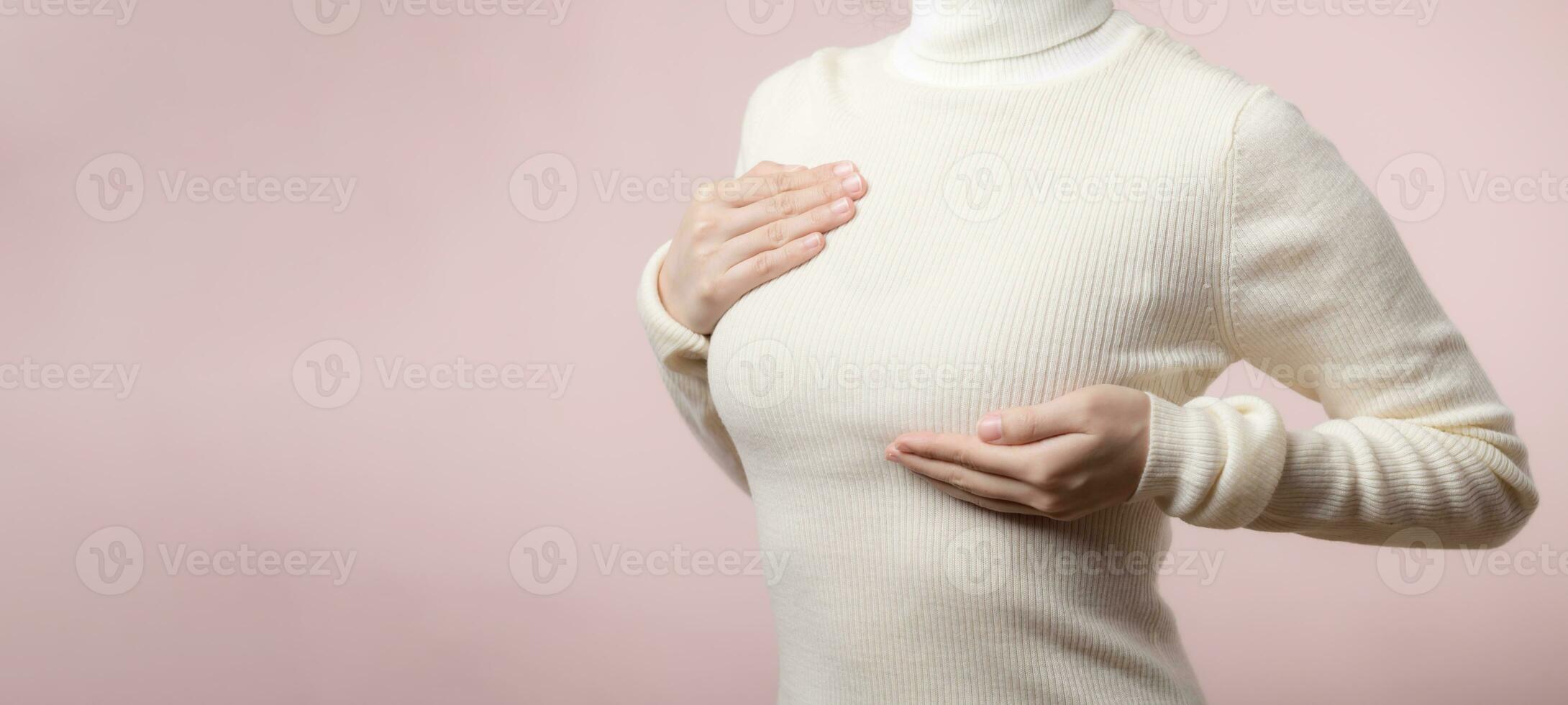 Woman hands checking lumps on her breast for signs of breast cancer on pink background. Healthcare world health day concept. photo