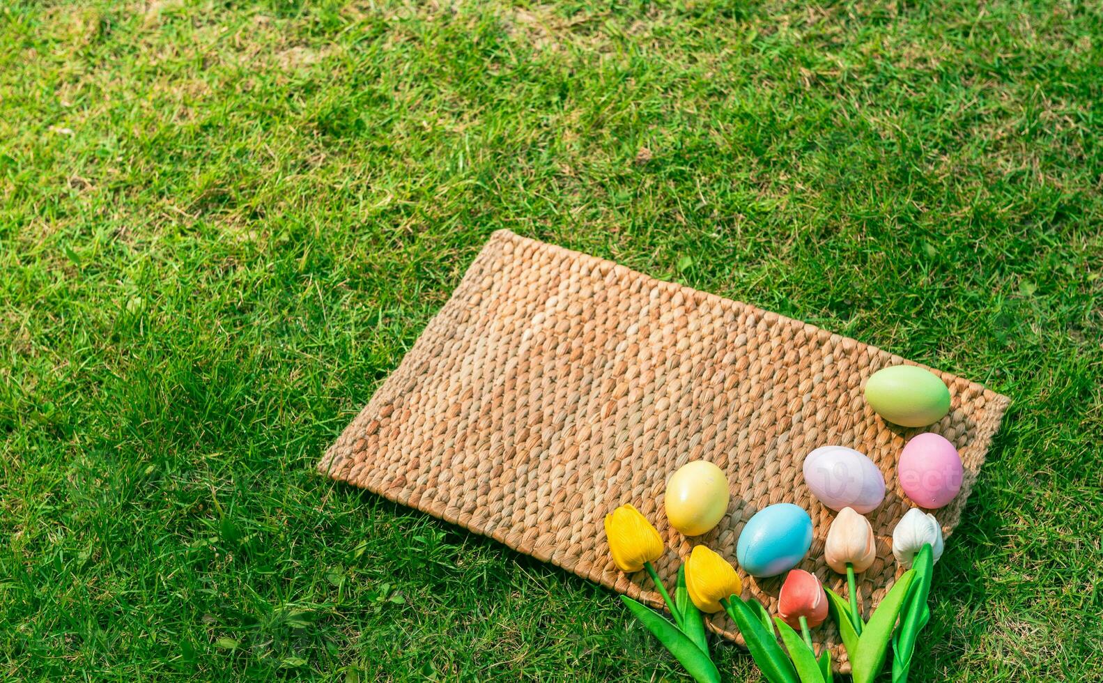Happy Easter holiday greeting card concept. Colorful Easter Eggs and spring flowers on Papyrus rattan weave texture background. Flat lay, top view, copy space. photo