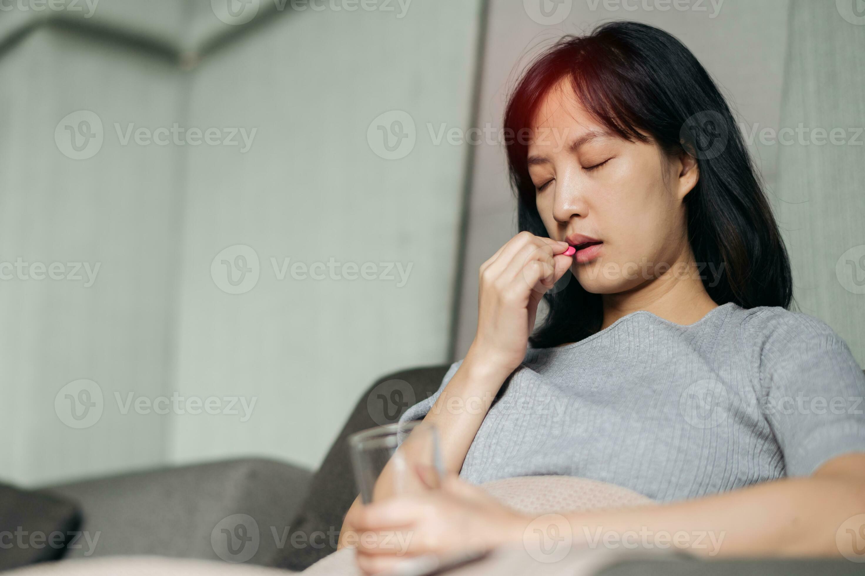Asian young woman take a medicine pill while laying on sofa at home
