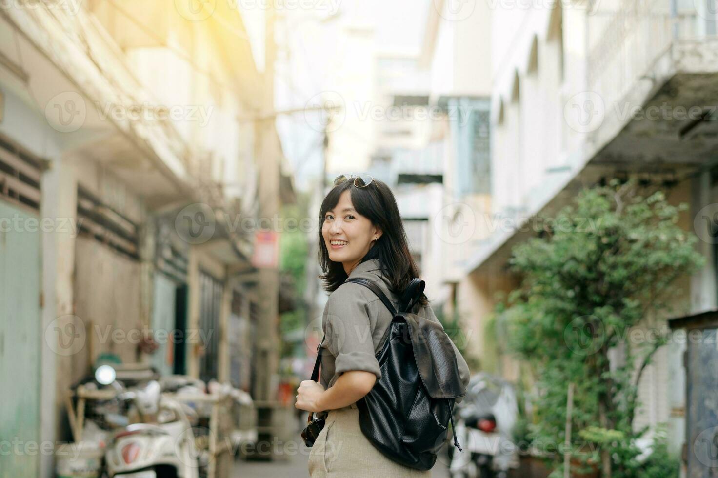 joven asiático mujer mochila viajero disfrutando calle cultural local sitio y sonrisa. viajero comprobación fuera lado calles foto