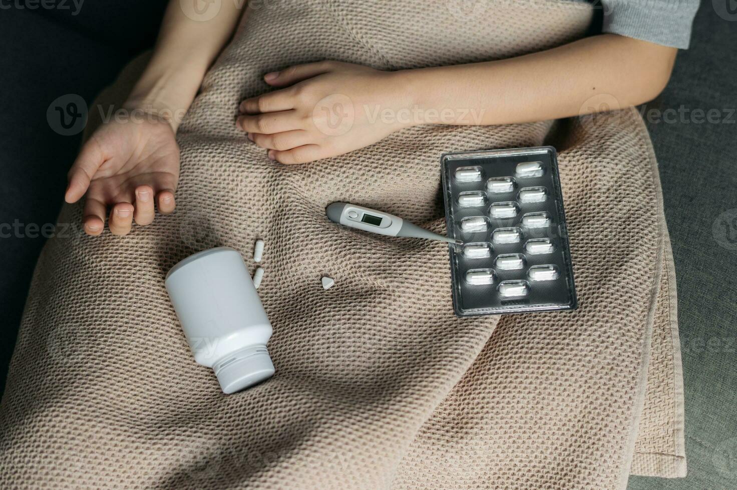 disease sick person under blanket with medicine, health temperature, pill, drug bottle over sofa bed at home. Fever ill woman with flu virus infection on medical care resting, lying in indoor bedroom. photo