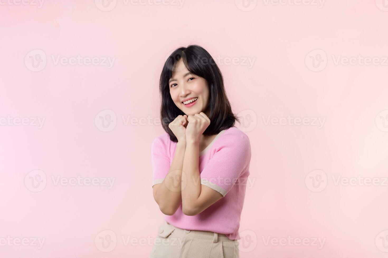 Adorable young happy asian woman model with shy emotion smiling expression cheerful positive attractive face and holding hand isolated on pink pastel studio background. Portrait beautiful cute lady. photo