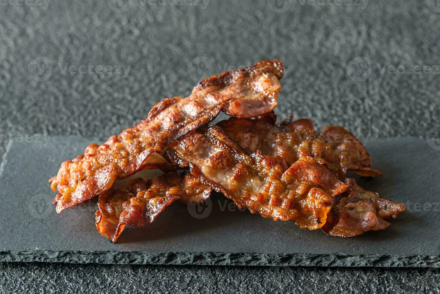 Fried bacon strips on the stone dark board photo