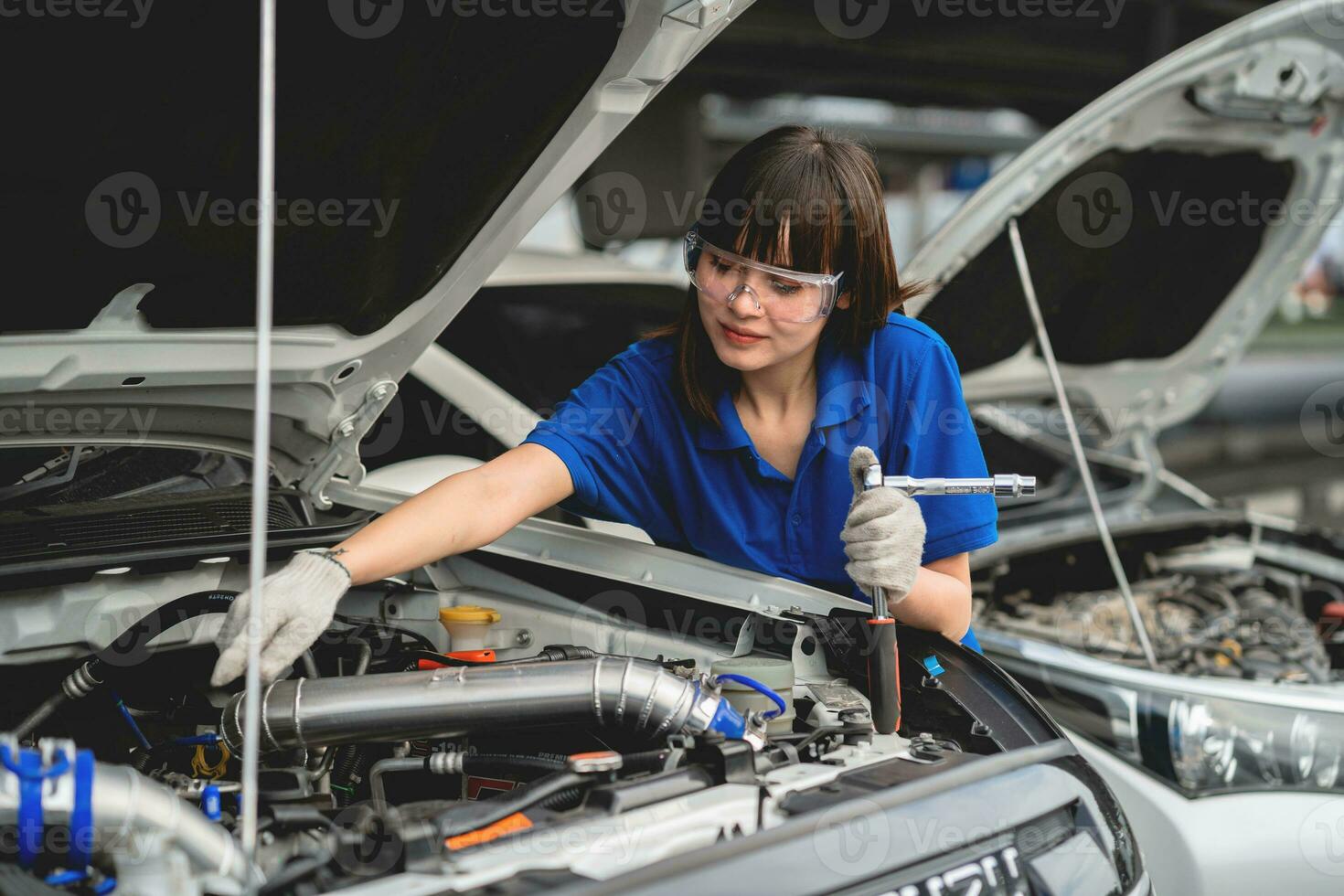 Female mechanic working in a car service. A woman wearing gloves and using a wheel under a workshop car. repair service concept Car repair and maintenance. photo