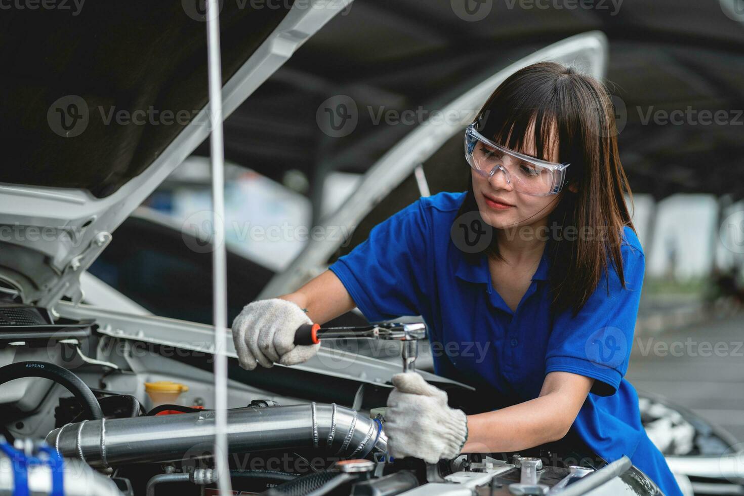 hembra auto mecánico abre coche capucha a inspeccionar motor dañar y realizar profesional mantenimiento él vistió un azul uniforme y inspeccionado y reparado su coche en el taller. foto