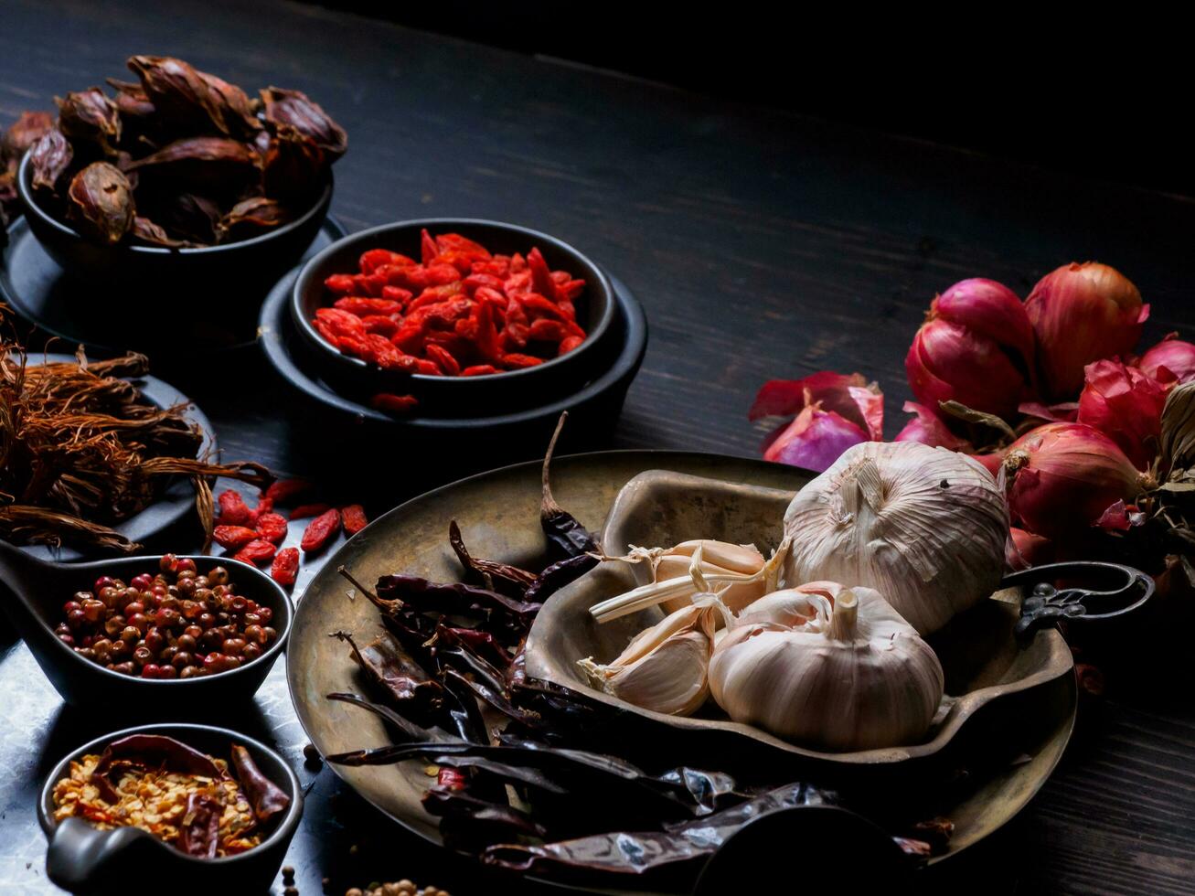 Top view photo Lots of garlic, onions, peppers, chili and dried herbs, were placed on plates and cups on a black wooden drak background. was divided To prepare to cook food india healthy food