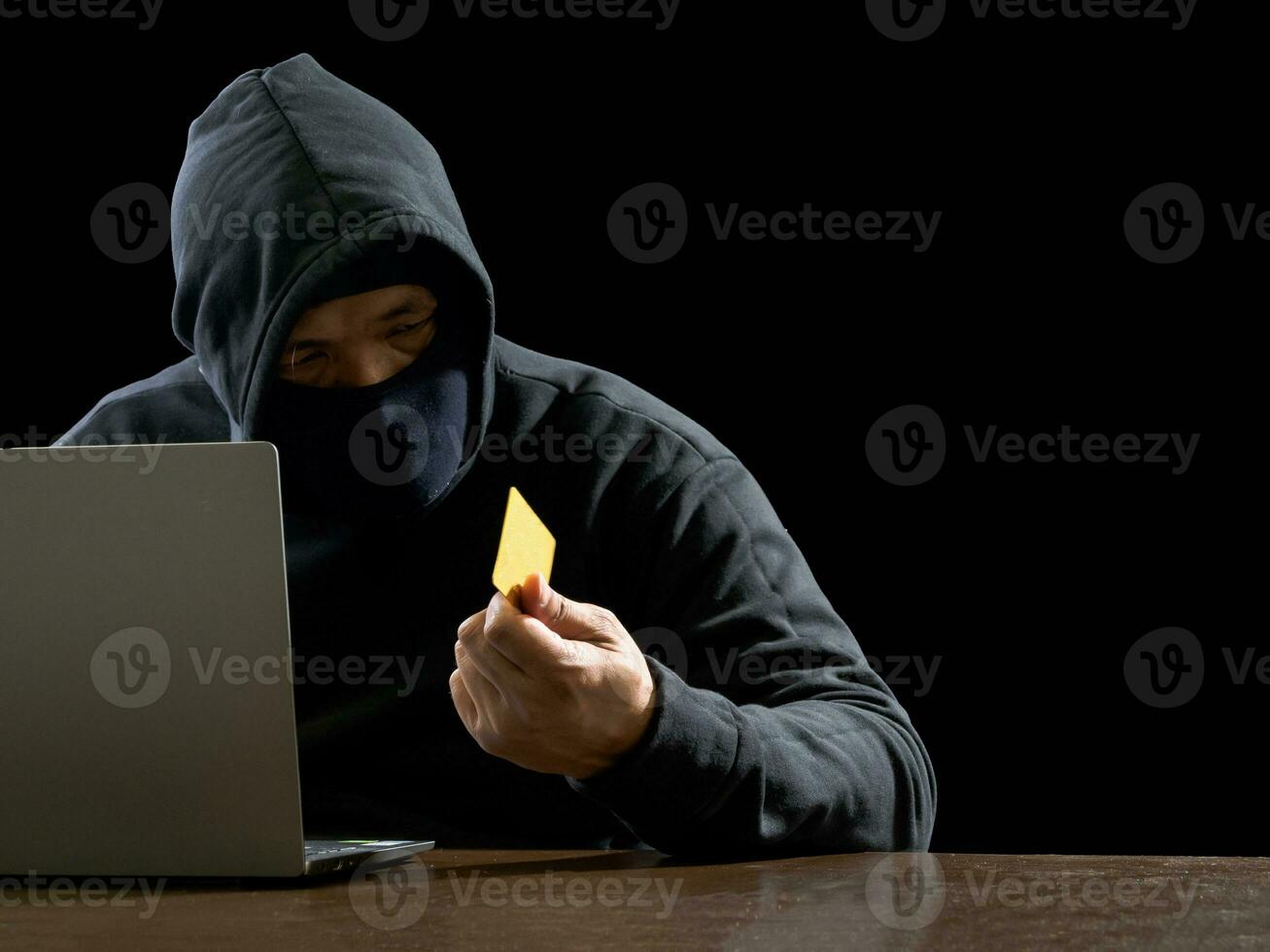Hacker spy man one person in black hoodie sitting on a table looking computer laptop used login password attack security to circulate data digital in internet network system, night dark background. photo