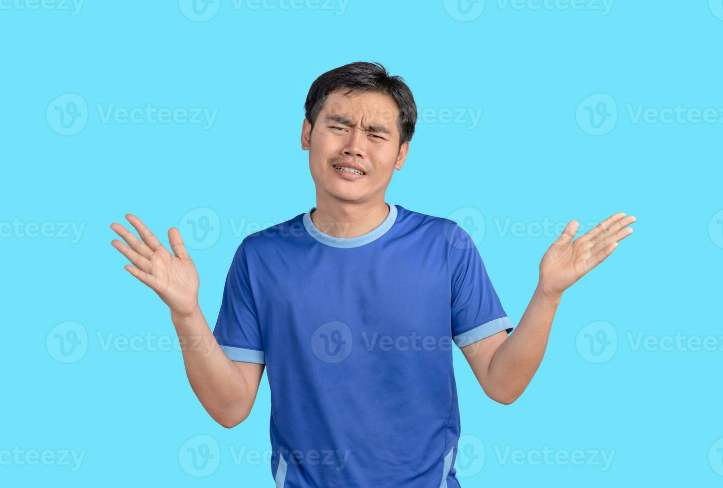 Doubtful young man shrugging with shoulders. Emotional man on blue background. I don't know, who cares. Confused clueless man in a blue t-shirt shrugging his shoulders, making no idea gesture. photo