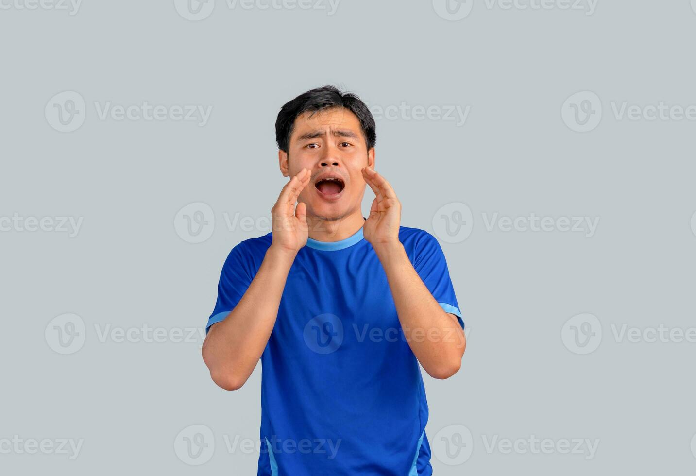 Portrait of a Happy young man keeping arms raised and looking at camera while standing against grey background. Sharing good news. photo