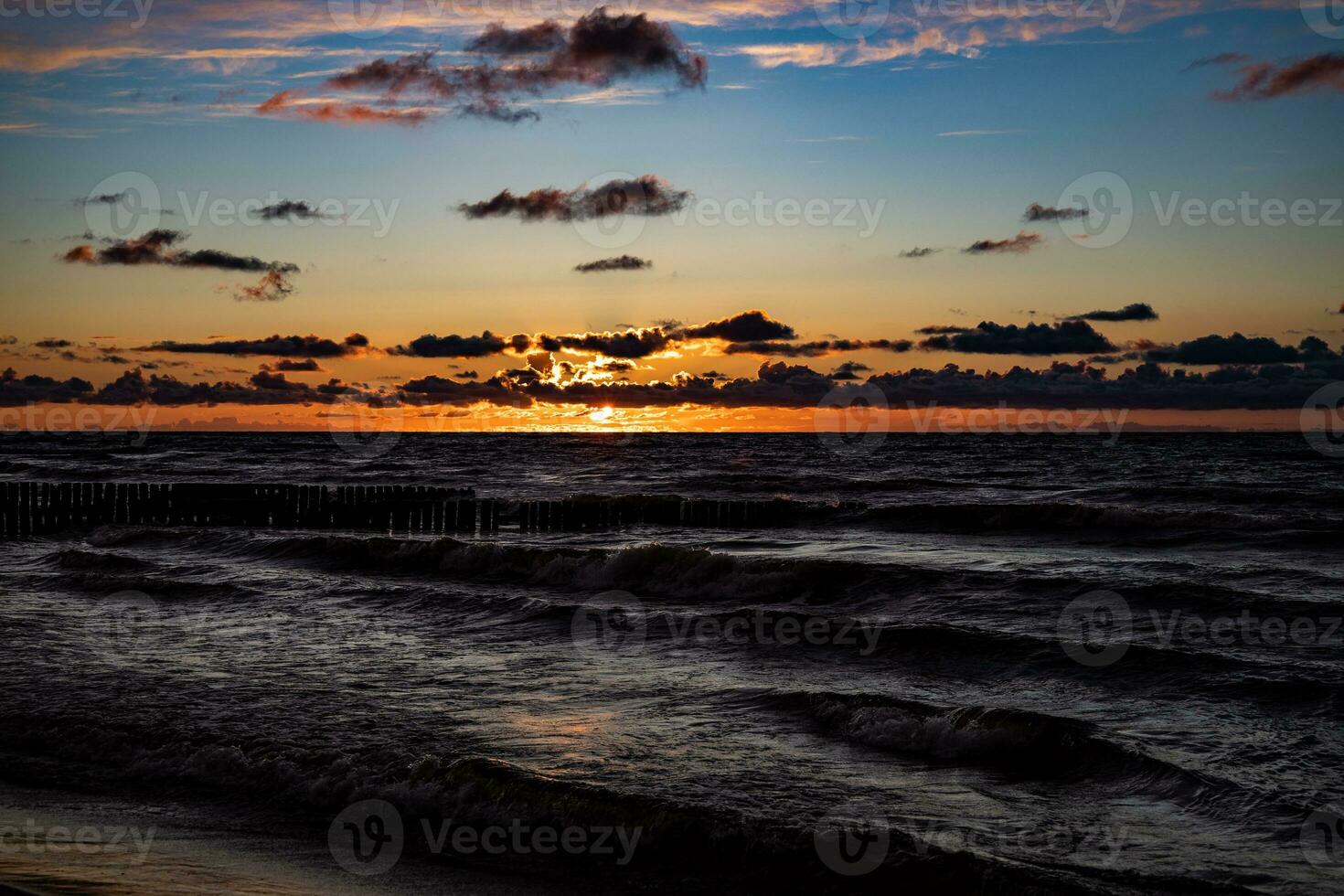 vistoso puesta de sol terminado el polaco báltico mar con oscuro cielo nubes y rompeolas foto