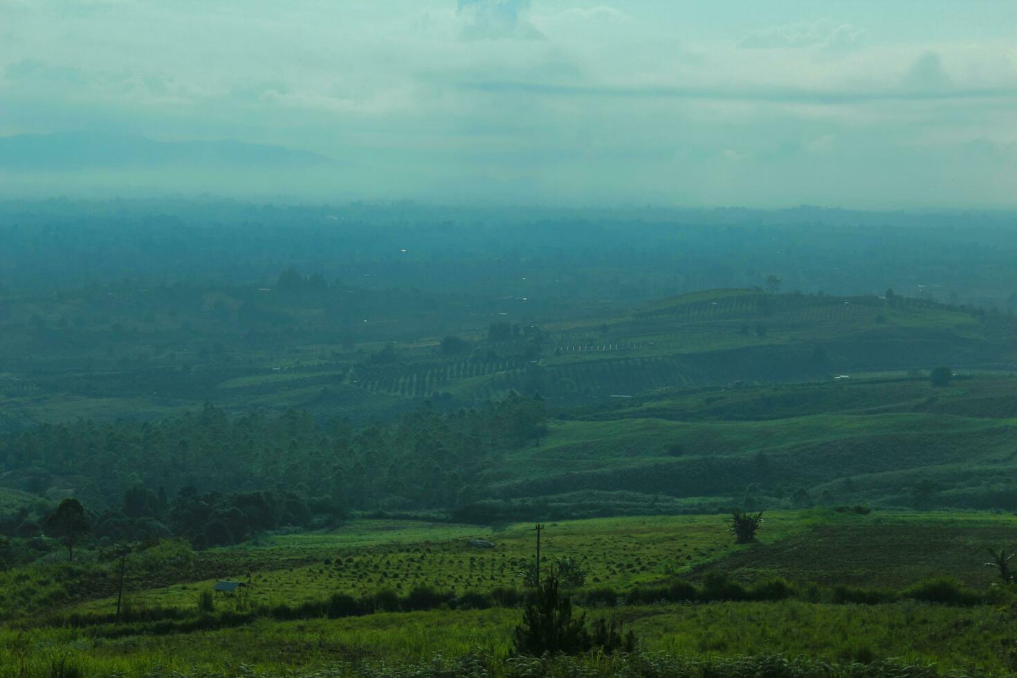 aerial view with beautiful green hills landscape.  a meadow with a cloud shadow and a distant layer of mountains in the air mist photo