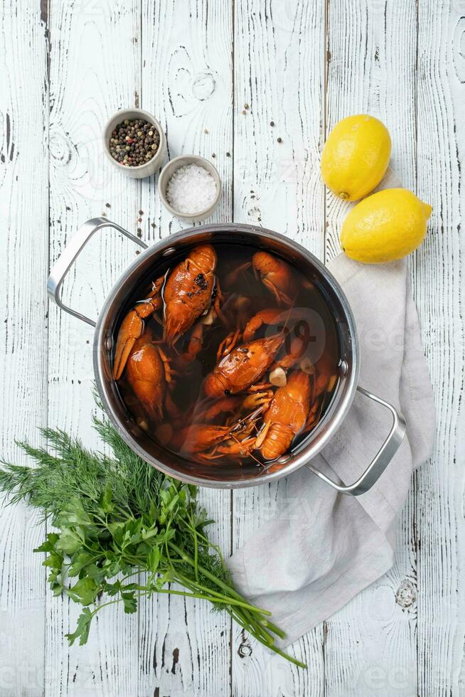 cooked crawfish in saucepan with lemons and spices on wooden background photo