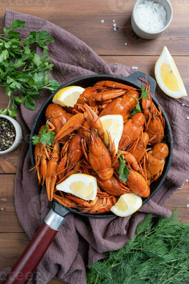 cooked crawfish in black saucepan with lemons and spices on wooden background photo