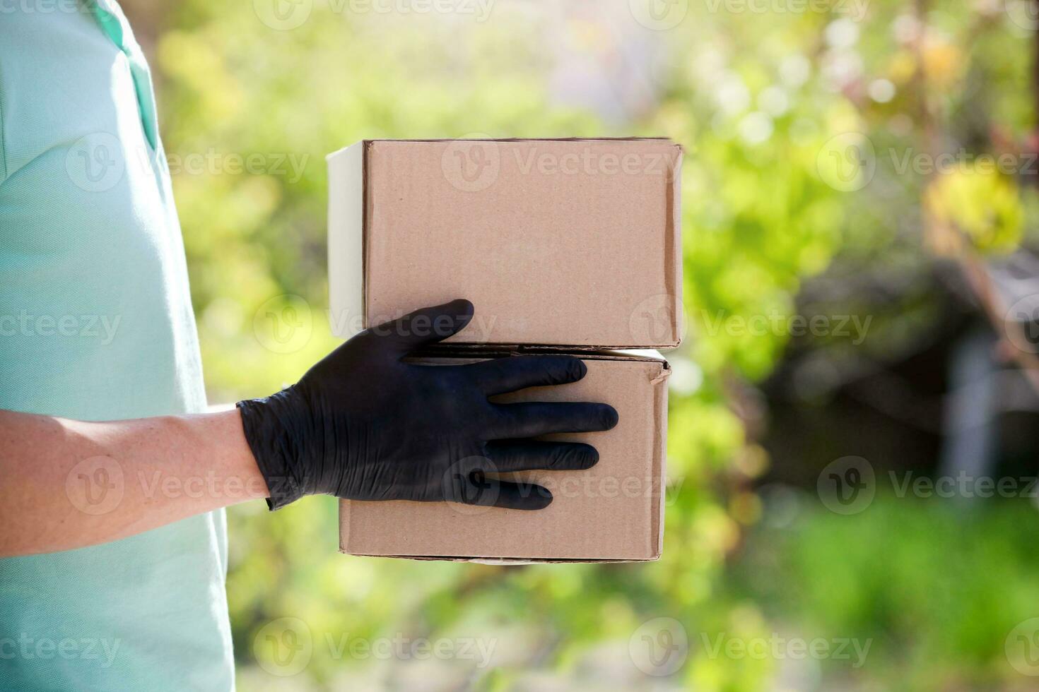 Delivery man holding cardboard boxes in medical rubber gloves at sunset on outdoor. photo