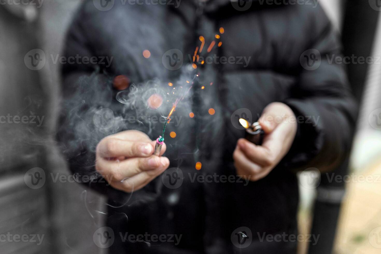 el petardo en un mano. chico participación un ardiente petardo en su mano. niño con un pirotécnica ese quemaduras con chispas y fumar al aire libre. petardo y encendedor en mano. foto