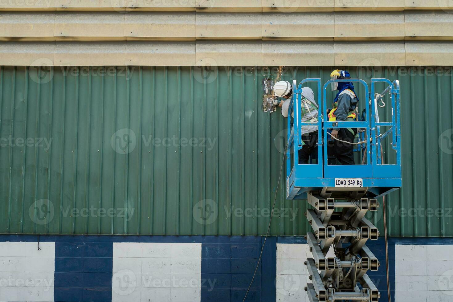 Two workers man on Scissor hydraulic lift or X-lift and use Electric wheel grinding or angle grinder on factory roof at a construction site, Mobile aerial work platform photo