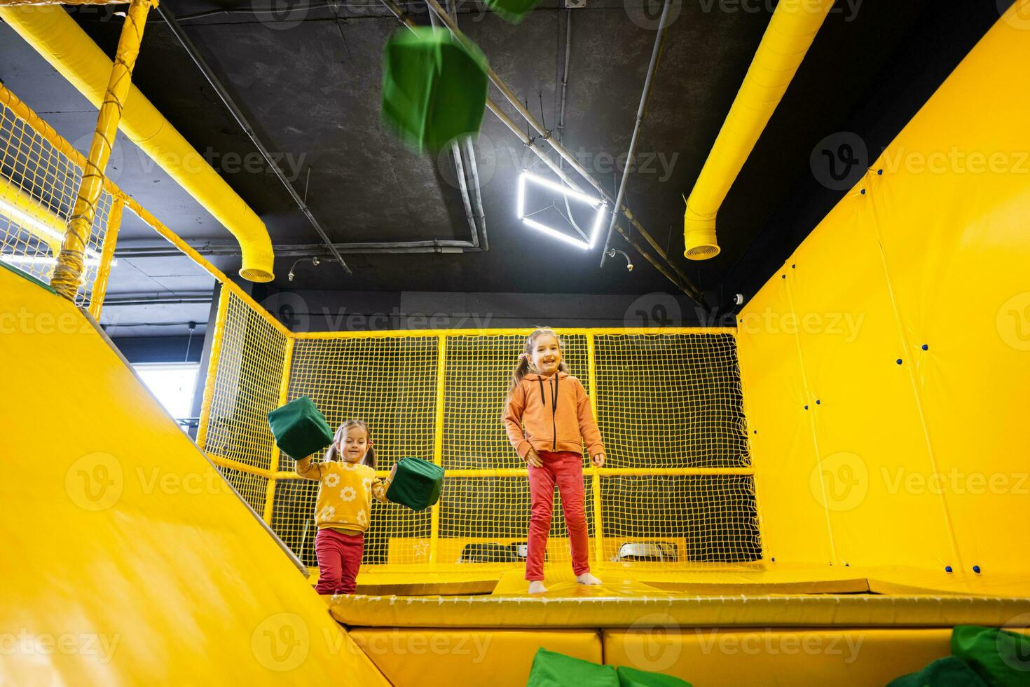 Siblings throwing soft cubes at yellow playground park. Sisters in active entertaiments. photo