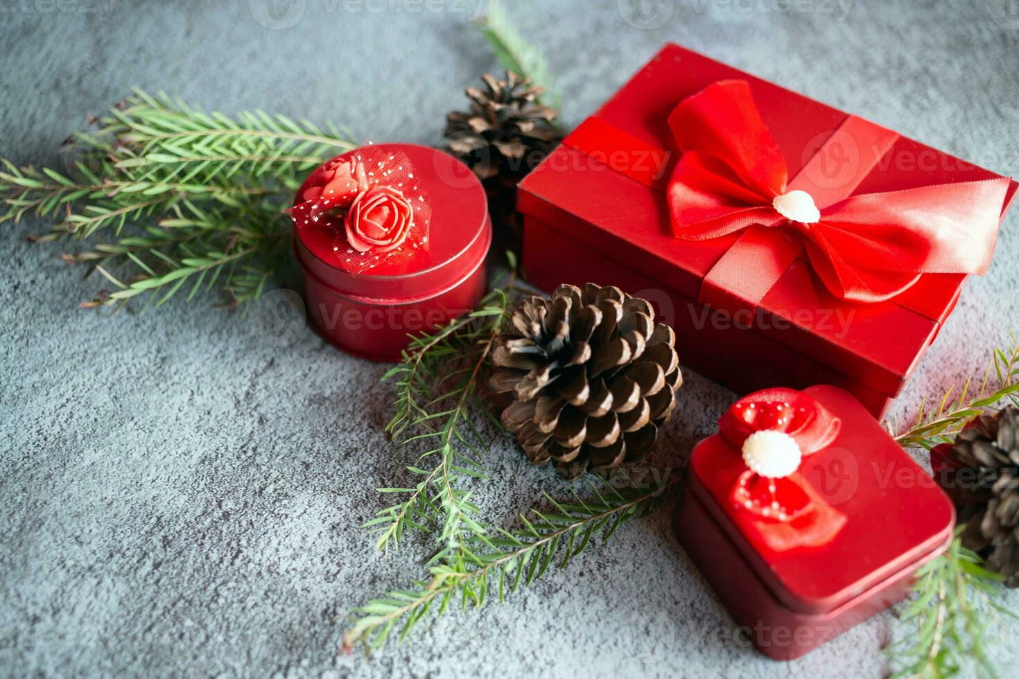 Christmas decoration composition on gray concrete background with a beautiful Red gift box with red ribbon, tree branches, and pine cones photo