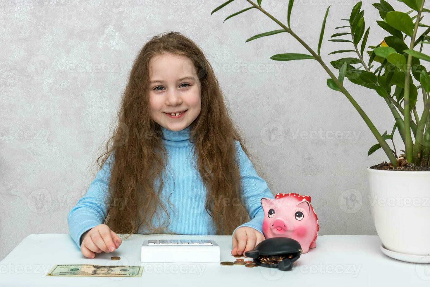 cute smiling girl sitting at the table counts money using a calculator from a piggy bank and a wallet, financial literacy photo