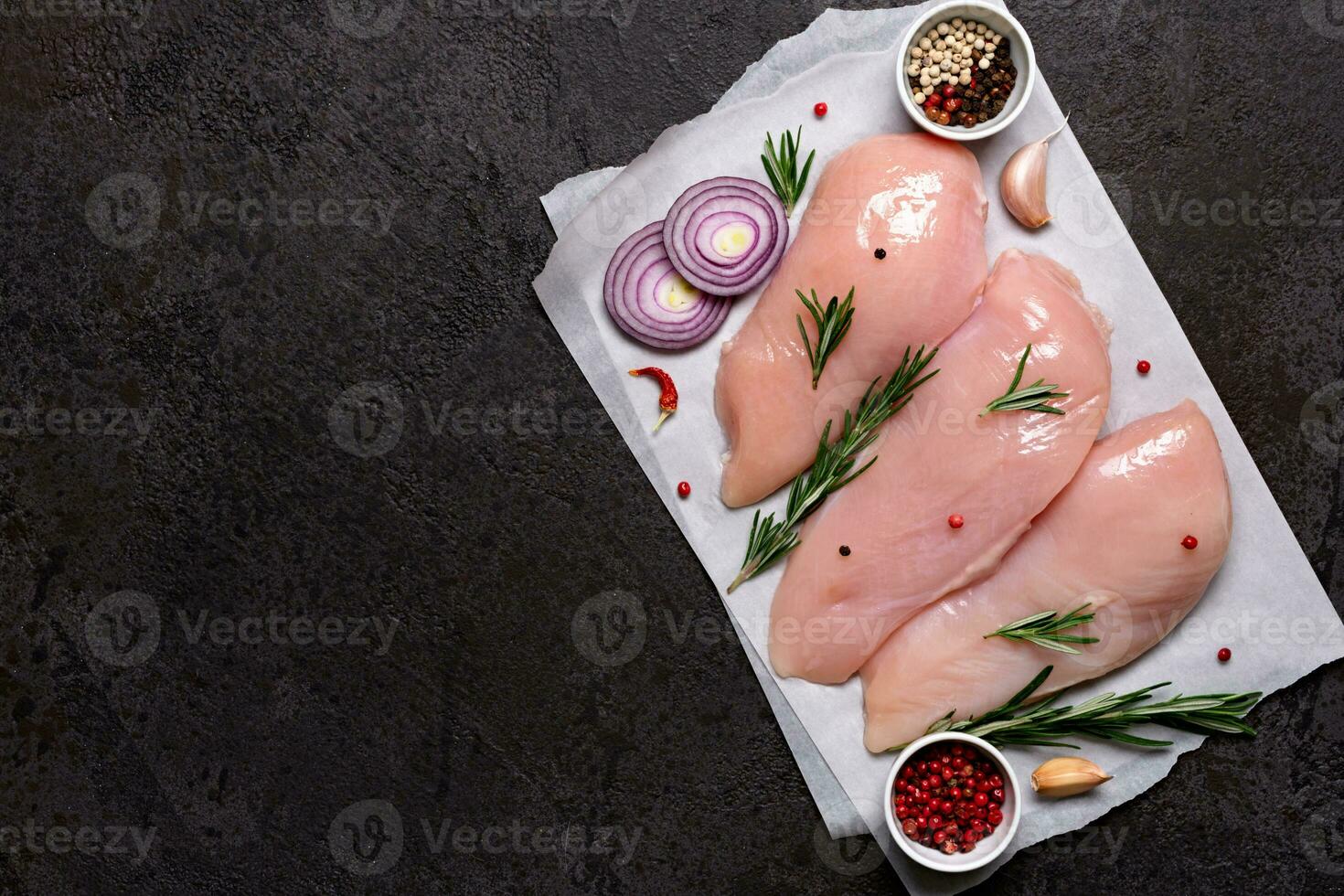 Fresh chicken breast fillet with spices and herbs on black stone background. Preparation for cooking photo