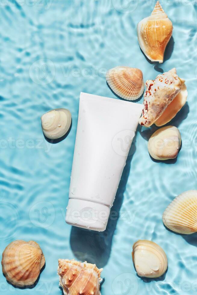 Organic cosmetic product with sea minerals. Skincare treatment cream or sun protection and shells on blue water background photo