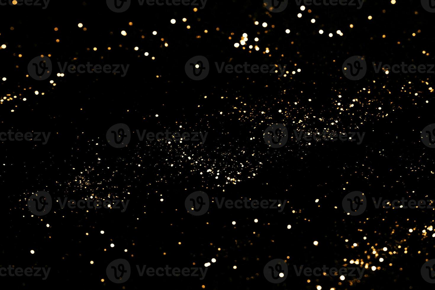 Black festive background. Abstract scattering of gold sparkles on black. Holiday backdrop, selective focus photo