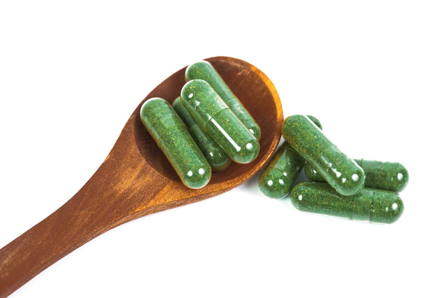 Herbal medicine capsules in wood spoon on white background photo