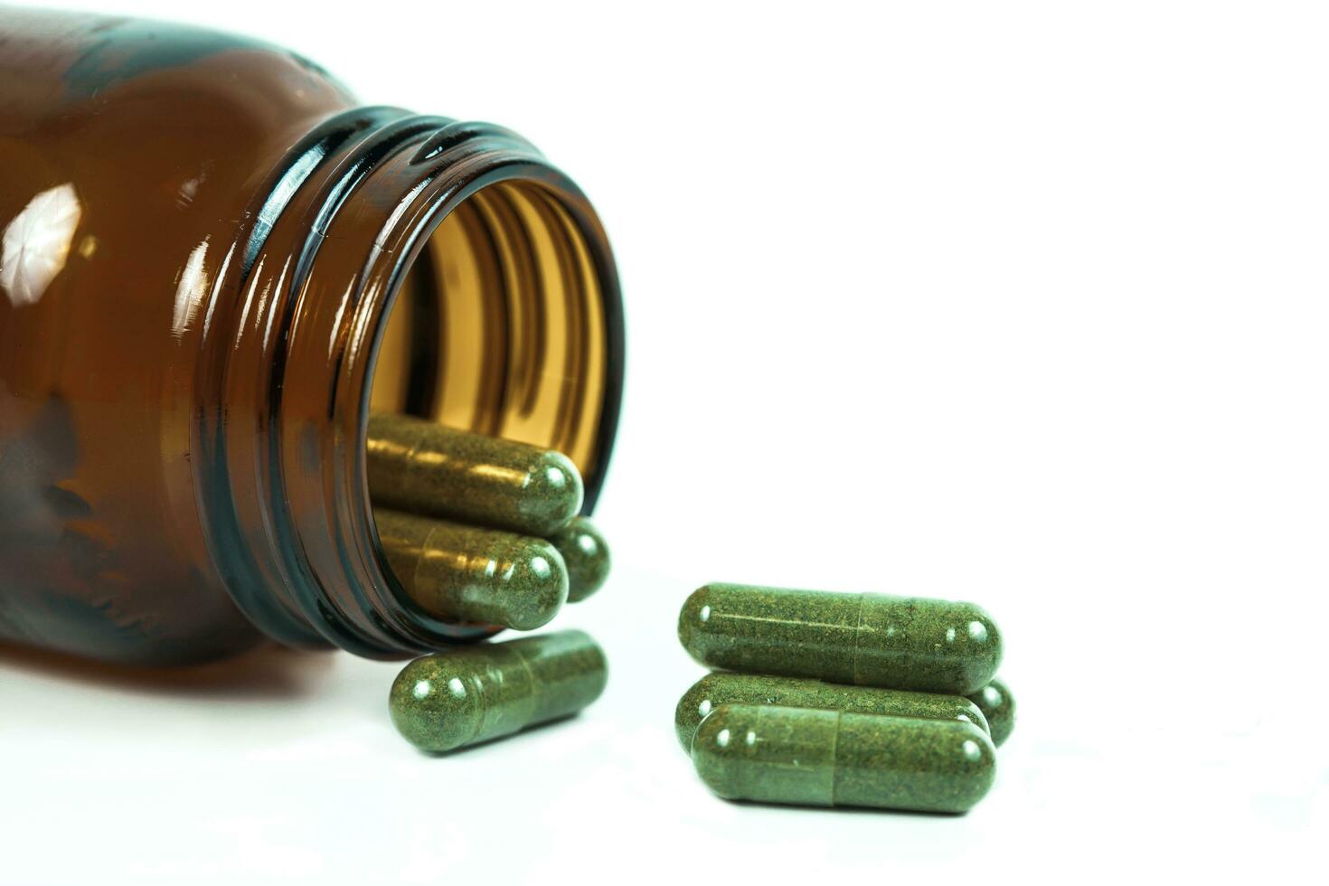 Herbal medicine capsules spilling out of a bottle on white photo