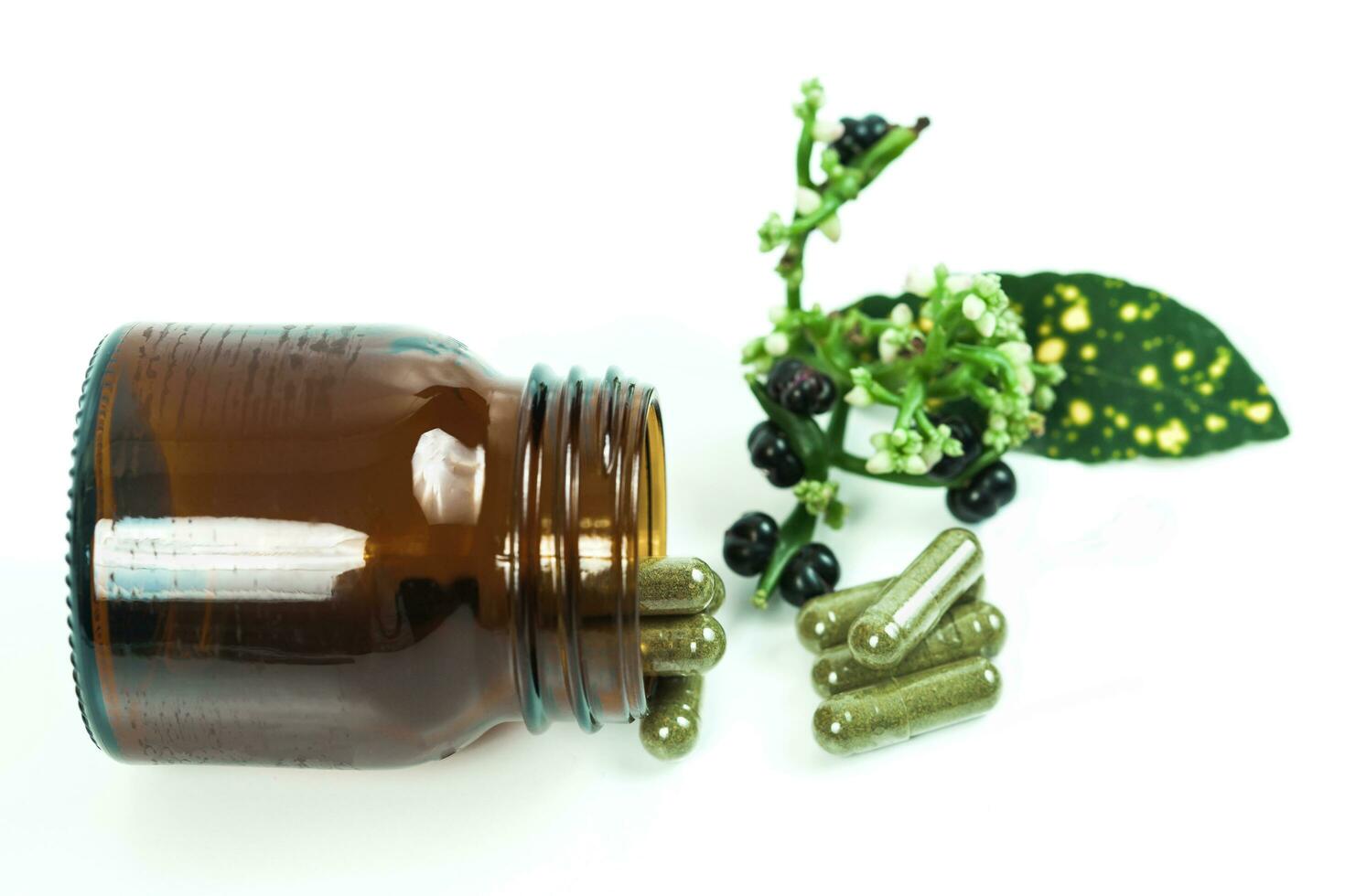 Herbal medicine capsules spilling out of a bottle on white photo