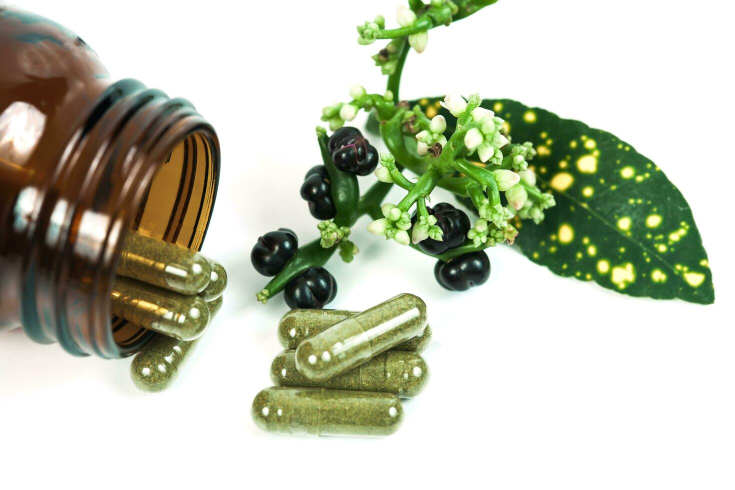 Herbal medicine capsules spilling out of a bottle on white photo