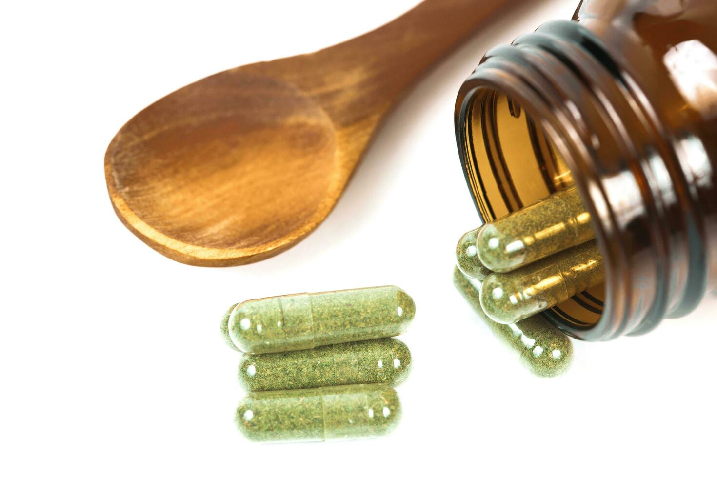 Herbal medicine capsules spilling out of a bottle on white photo