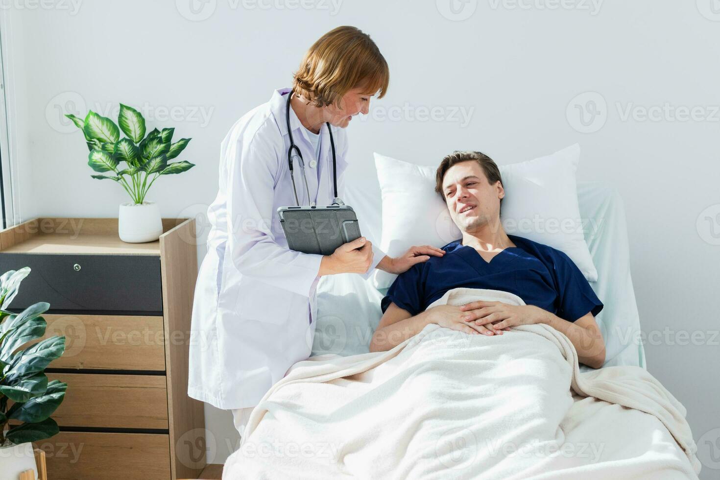 the doctor is examining the patient in the hospital. Caucasian female doctor talking to male patient lying in hospital bed. photo