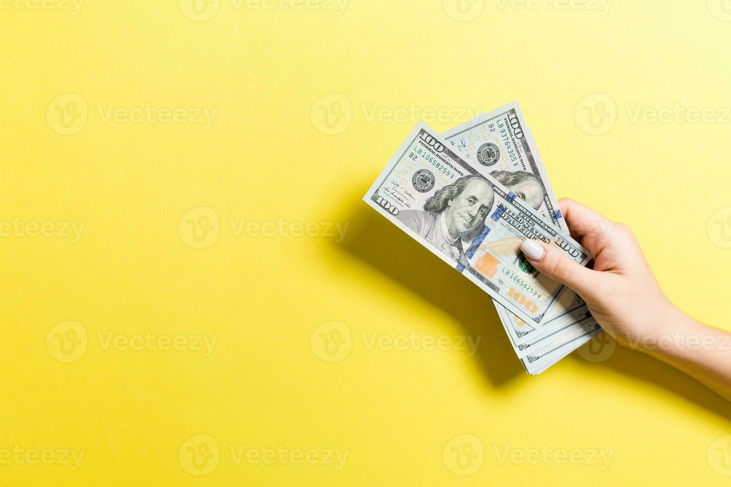 Female hand holding a bundle of money on colorful background. Top view of one hundred dollar banknotes. Salary concept with empty space for your design photo